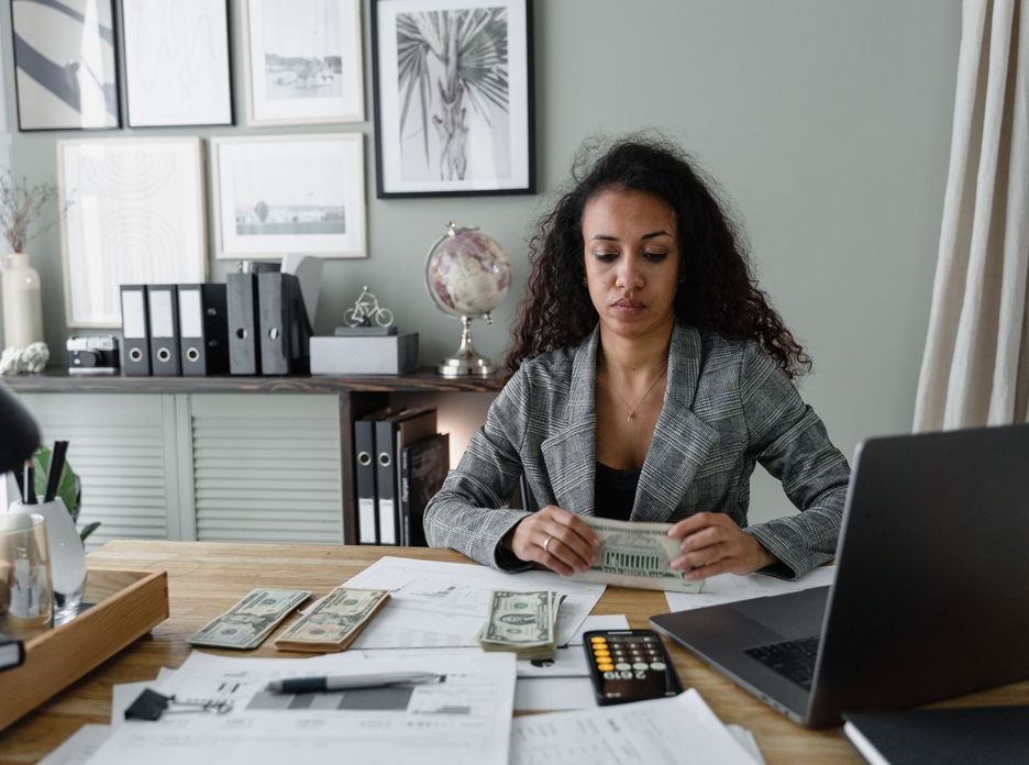 Focused woman counts cash at desk surrounded by office items