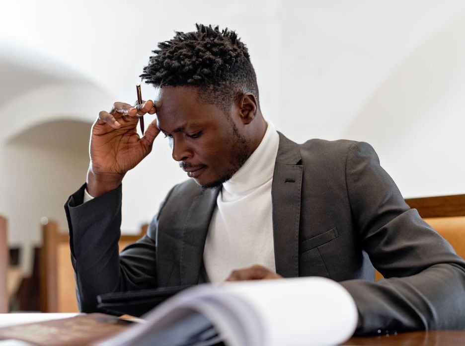 A focused businessman in a suit examines documents while deep in thought in an office setting