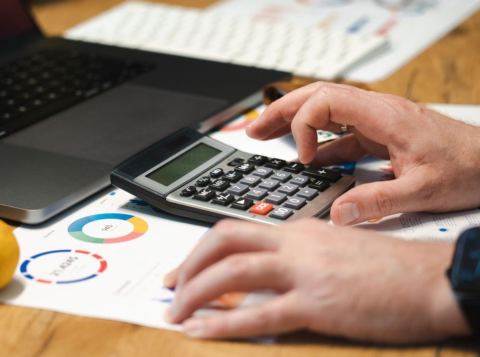A person analyzing financial data using a calculator and laptop on a desk