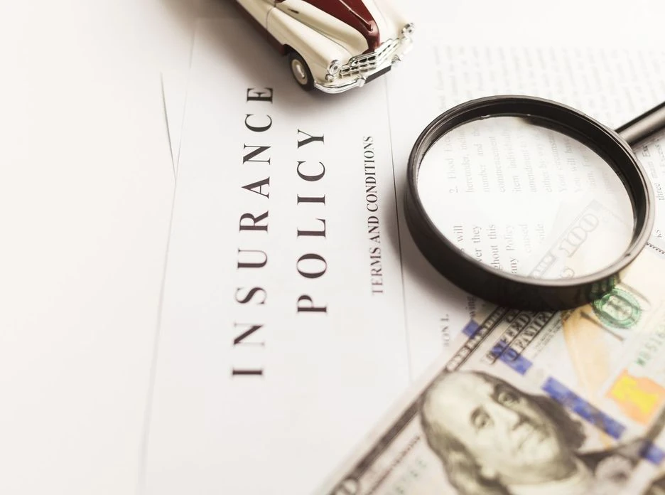 Close-up image of an insurance policy with a magnifying glass, money, and toy car