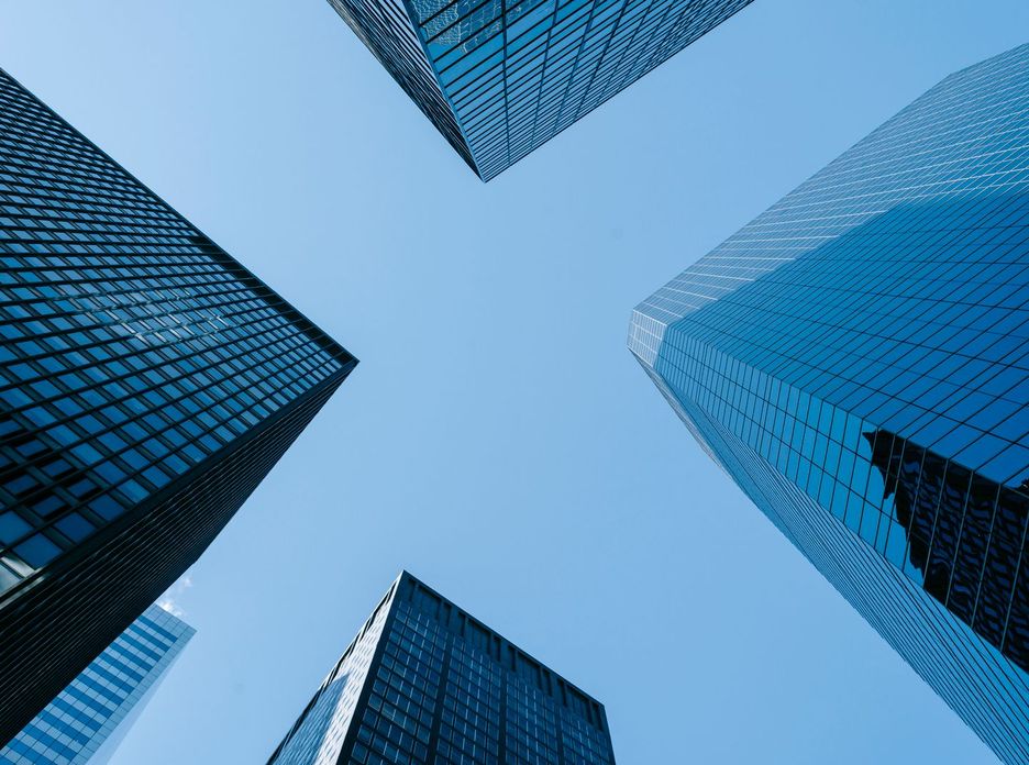 Low angle of high business towers with glass mirrored windows located in megalopolis downtown against blue sky