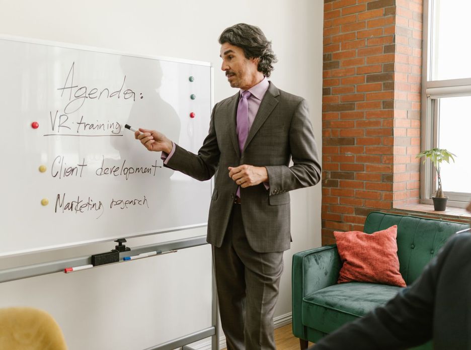 Businessman presenting a whiteboard agenda on VR training in modern office meeting