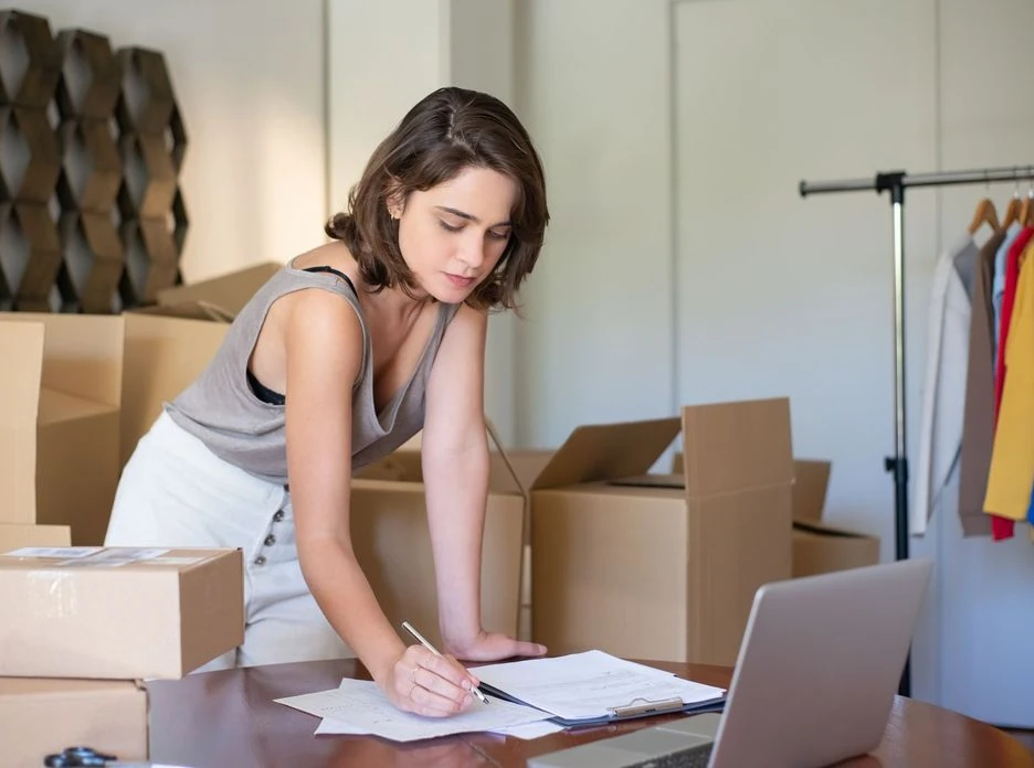 Young woman managing her online clothing business from home office with boxes and laptop
