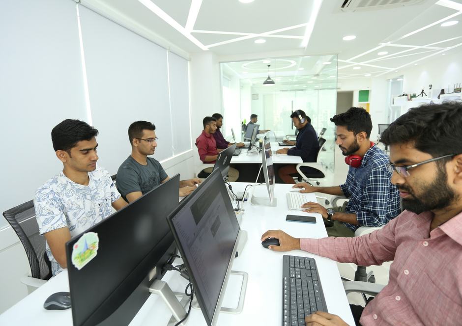 A team of men working at computers along rows of desks in a bright white office