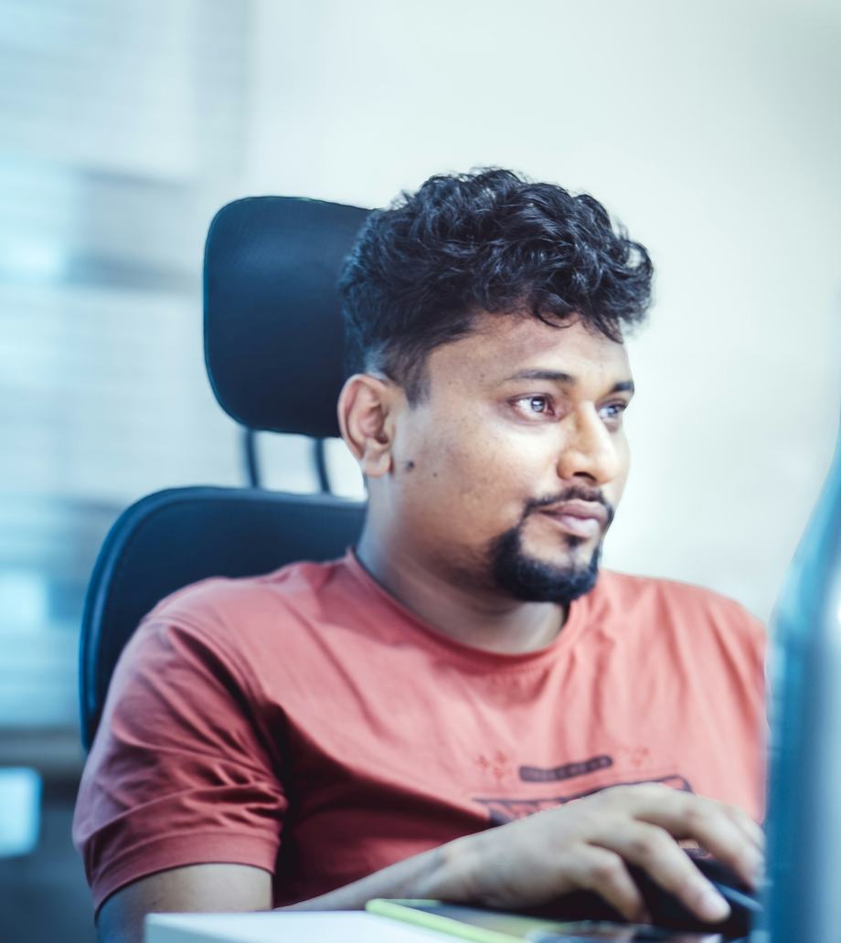 A man in a red T-shirt working at a computer in an office