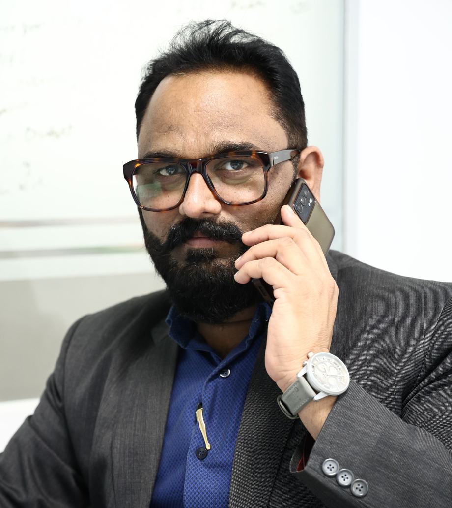 A bearded man in glasses and a grey suit on a phone call in an office