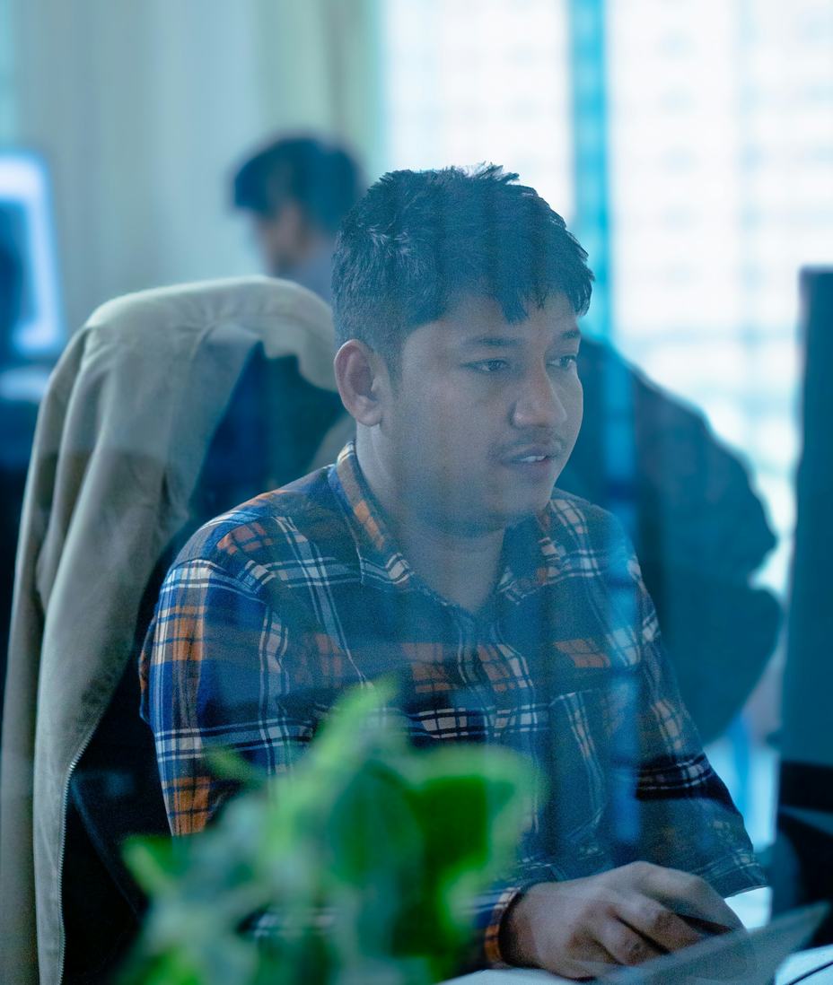 A young man in a plaid shirt working at a computer in an open office