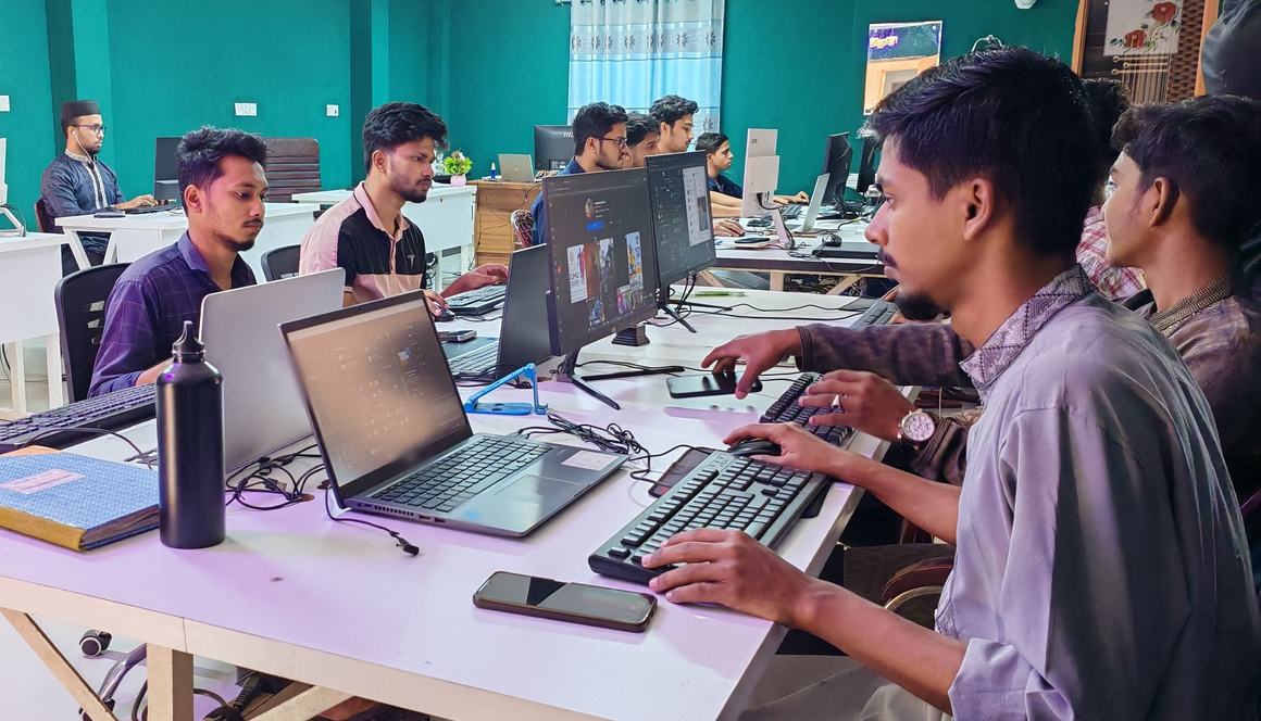 Young professionals working at laptops and computers along shared desks in an office with green walls